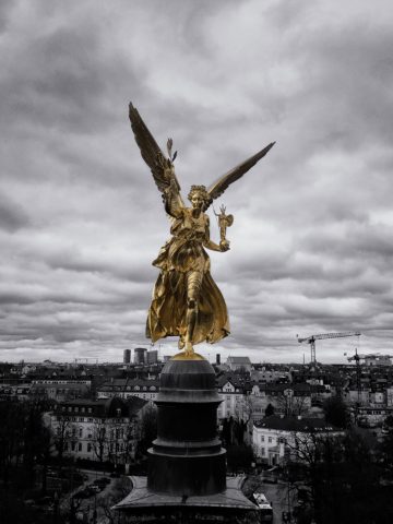 Der Friedensengel in Gold vor Münchens Stadtbild in schwarz-weiß. Fotografie von James Murray.
